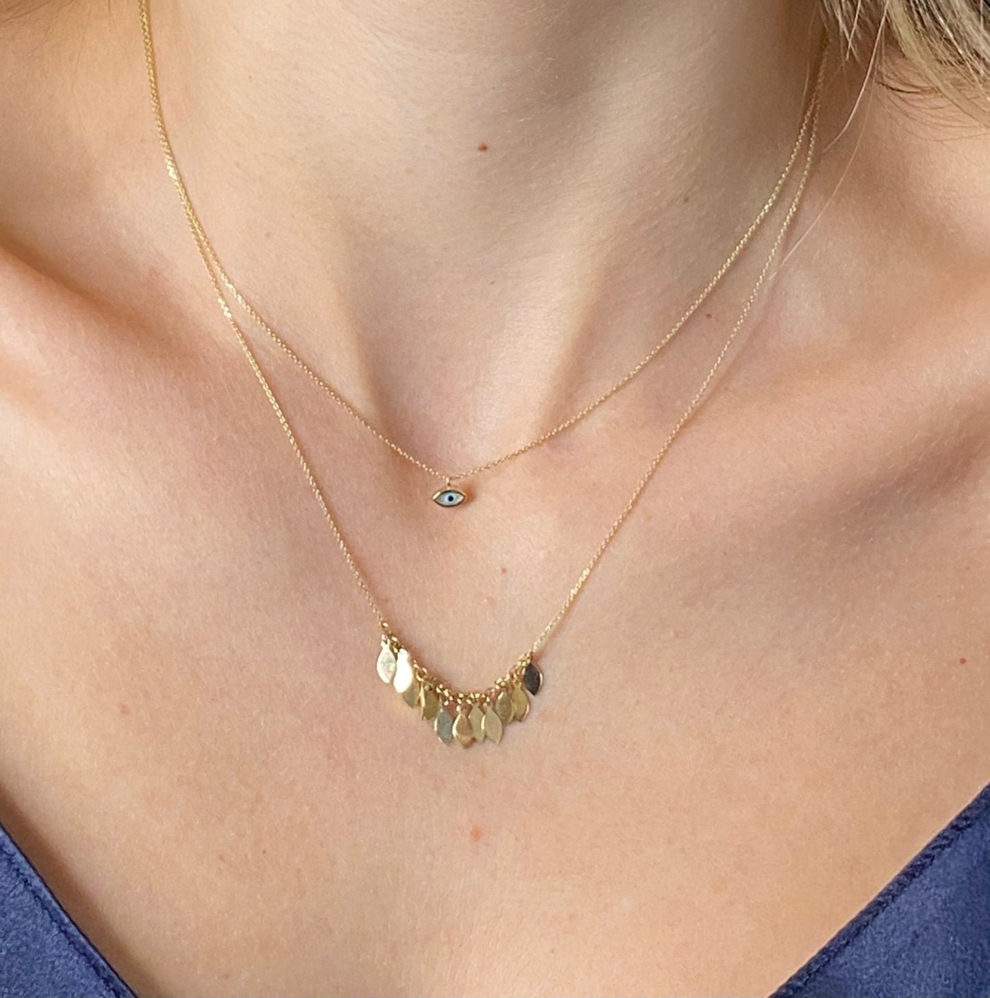 Tiny mother-of-pearl evil eye necklace in 14k gold and a 14k gold necklace with leaves worn by a model
