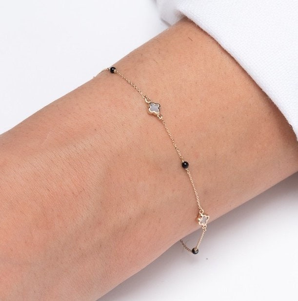 14k gold bracelet with four colver charms and three black onyx beads worn by a model