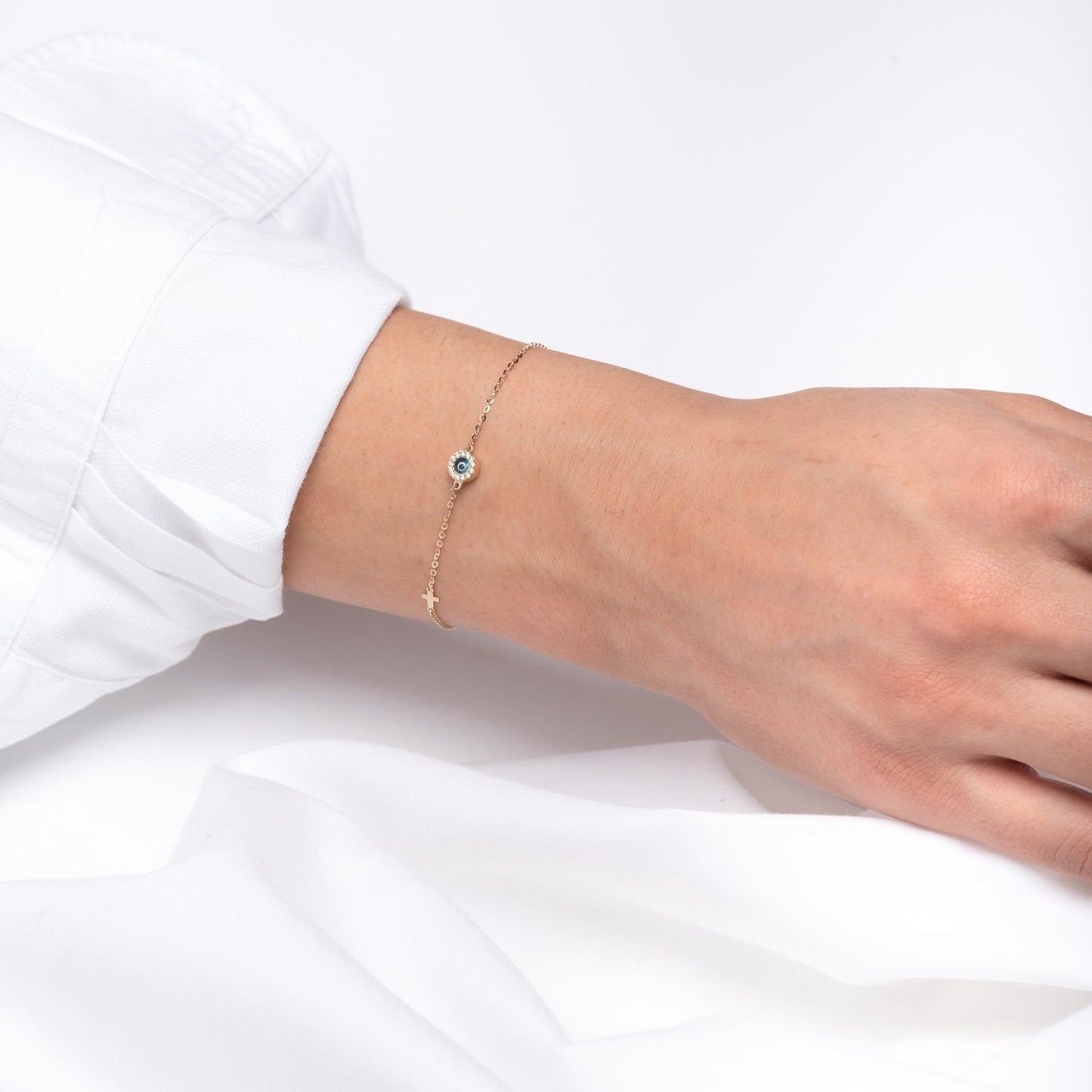 round evil eye bracelet with mourano glass and cubic zirconia stones and a small cross worn by a model