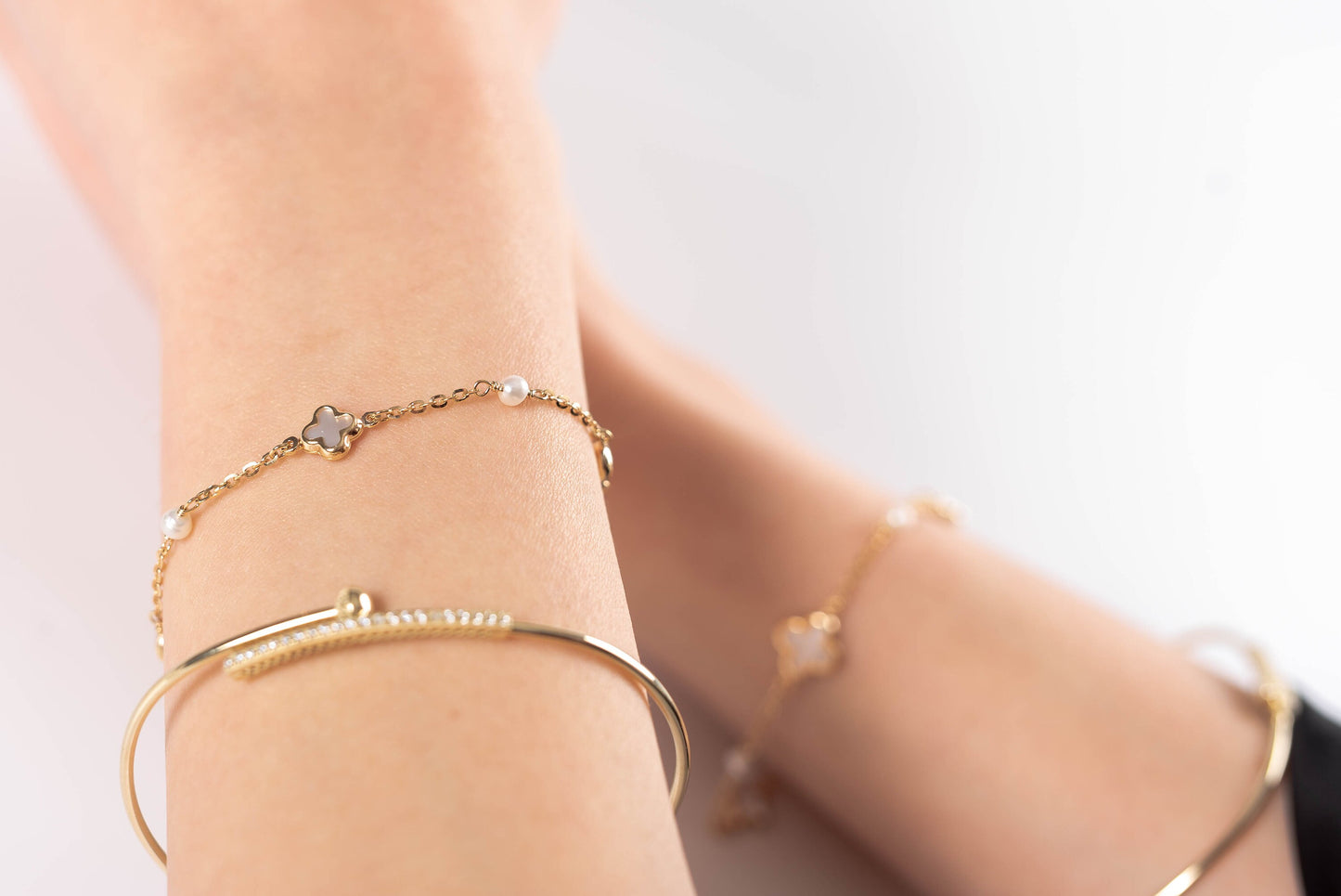 This is an image featuring several gold bracelets on a person's wrist. The bracelets vary in style, including a delicate chain bracelet, and a couple of minimalist bangle designs