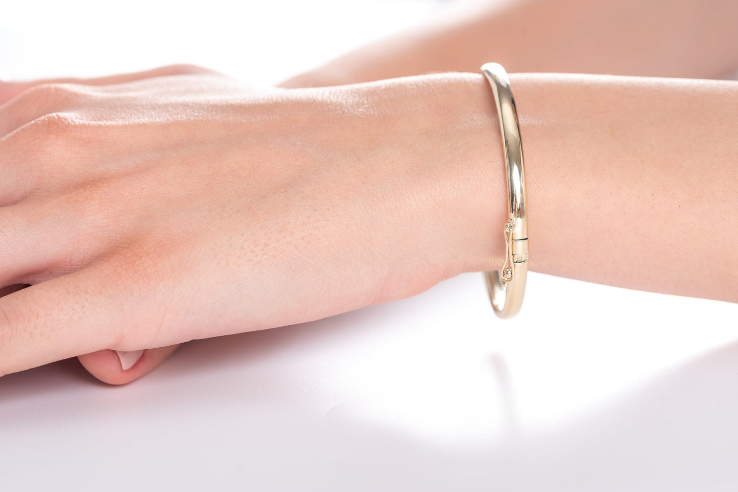 A hinged 4.20mm gold bangle bracelet made of 14k gold, displayed on a wrist.