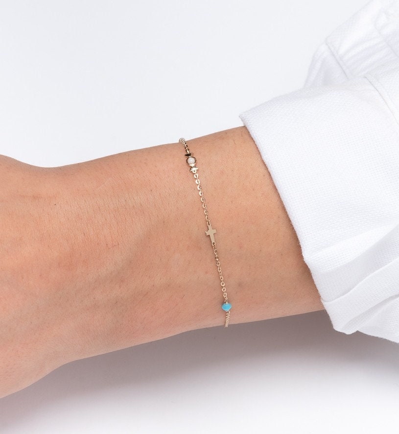 a hand wearing a 14k gold charm bracelet with star, candy, cross, pealr, turquoise