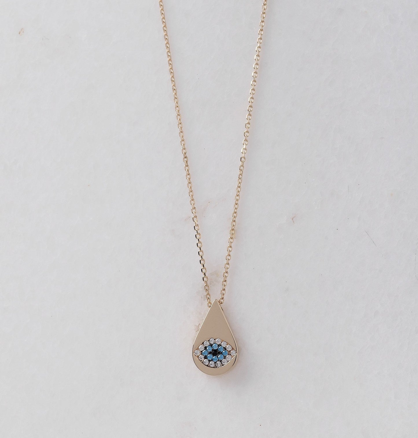 A drop-shaped evil eye necklace, encrusted with cubic zirconia stones and set in 14k gold.