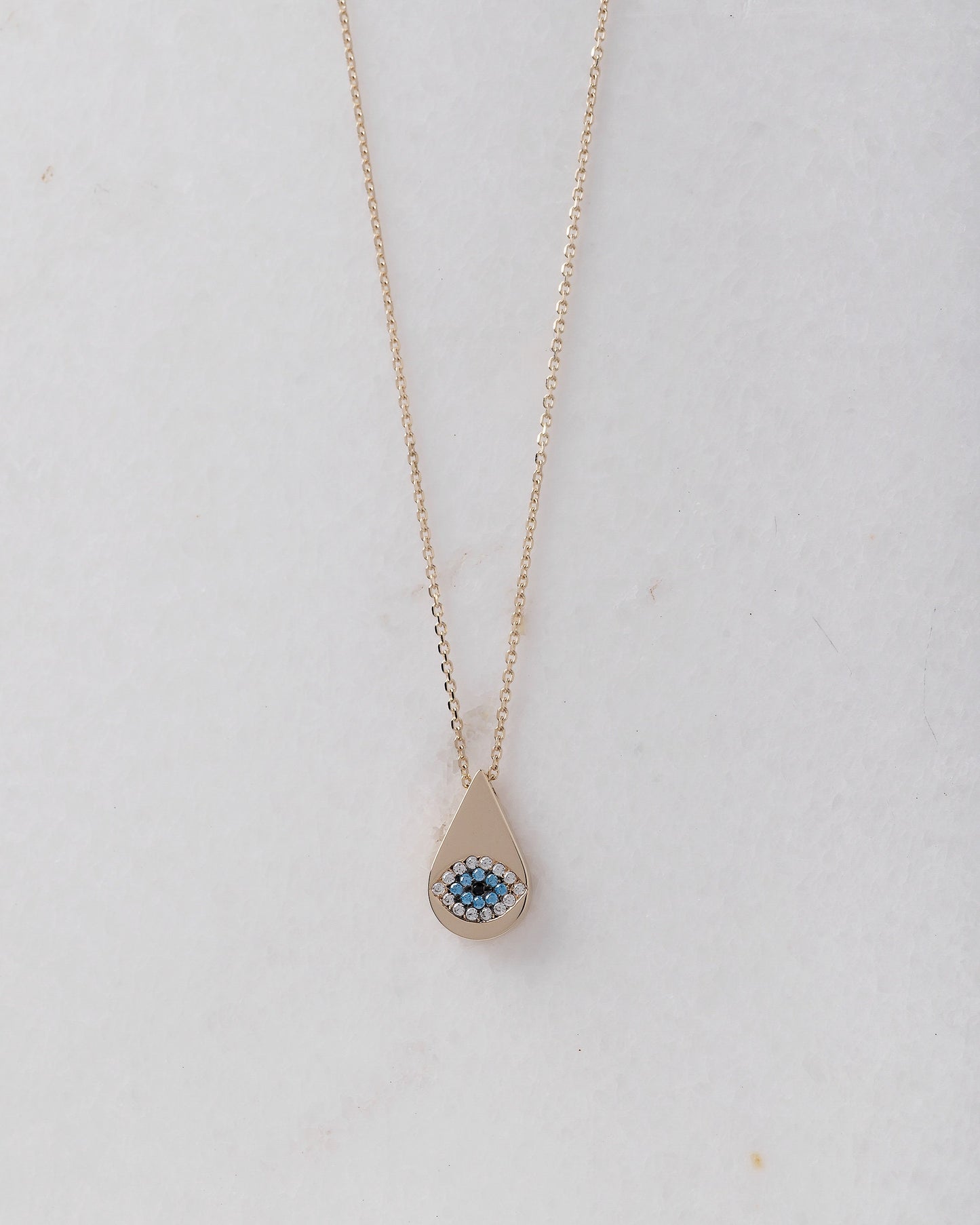 A drop-shaped evil eye necklace, encrusted with cubic zirconia stones and set in 14k gold.