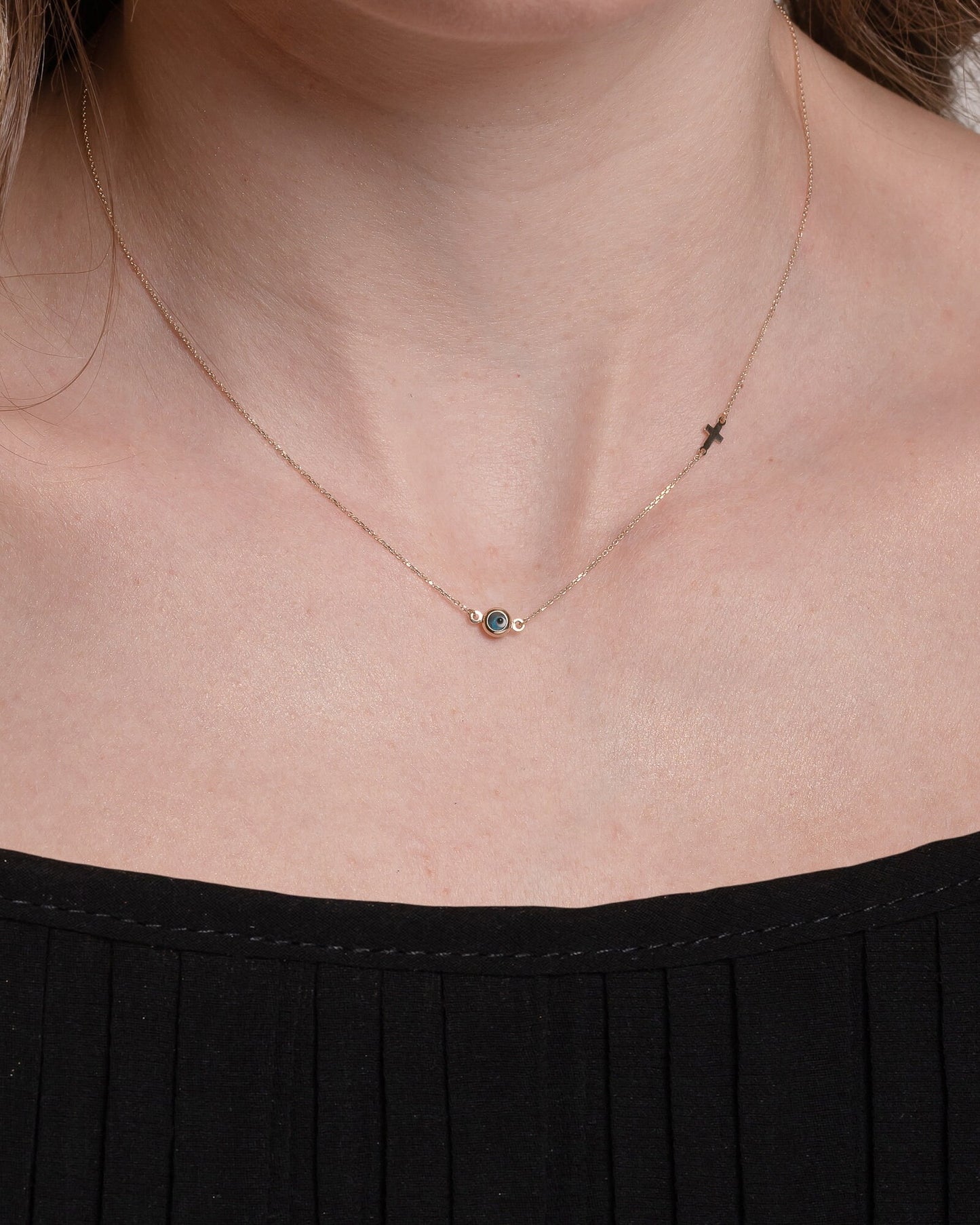 Murano glass double-sided evil eye necklace in 14k gold with a small side cross worn by a model
