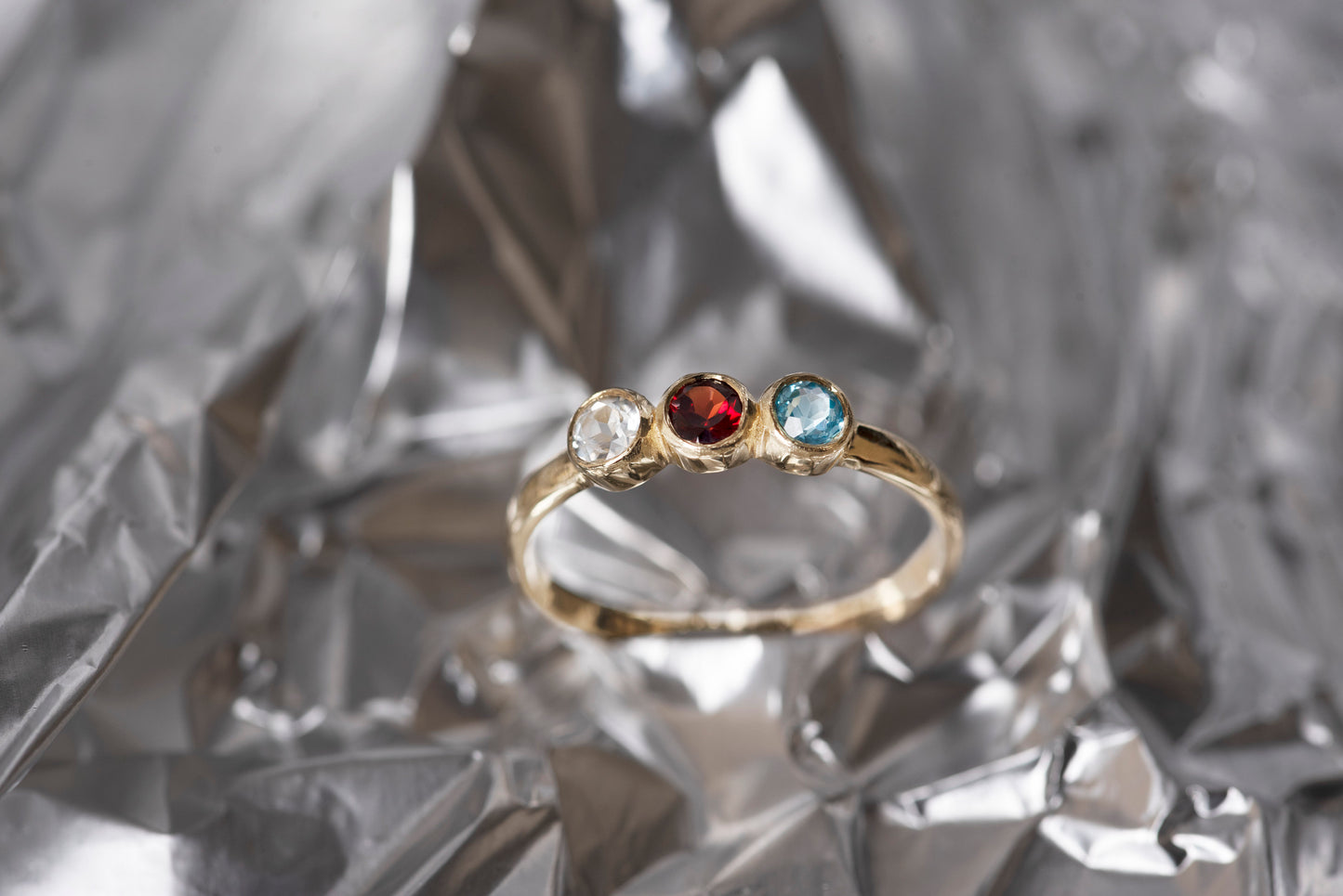 A handmade ring featuring three birthstones set in a bezel, crafted in 14k solid gold.