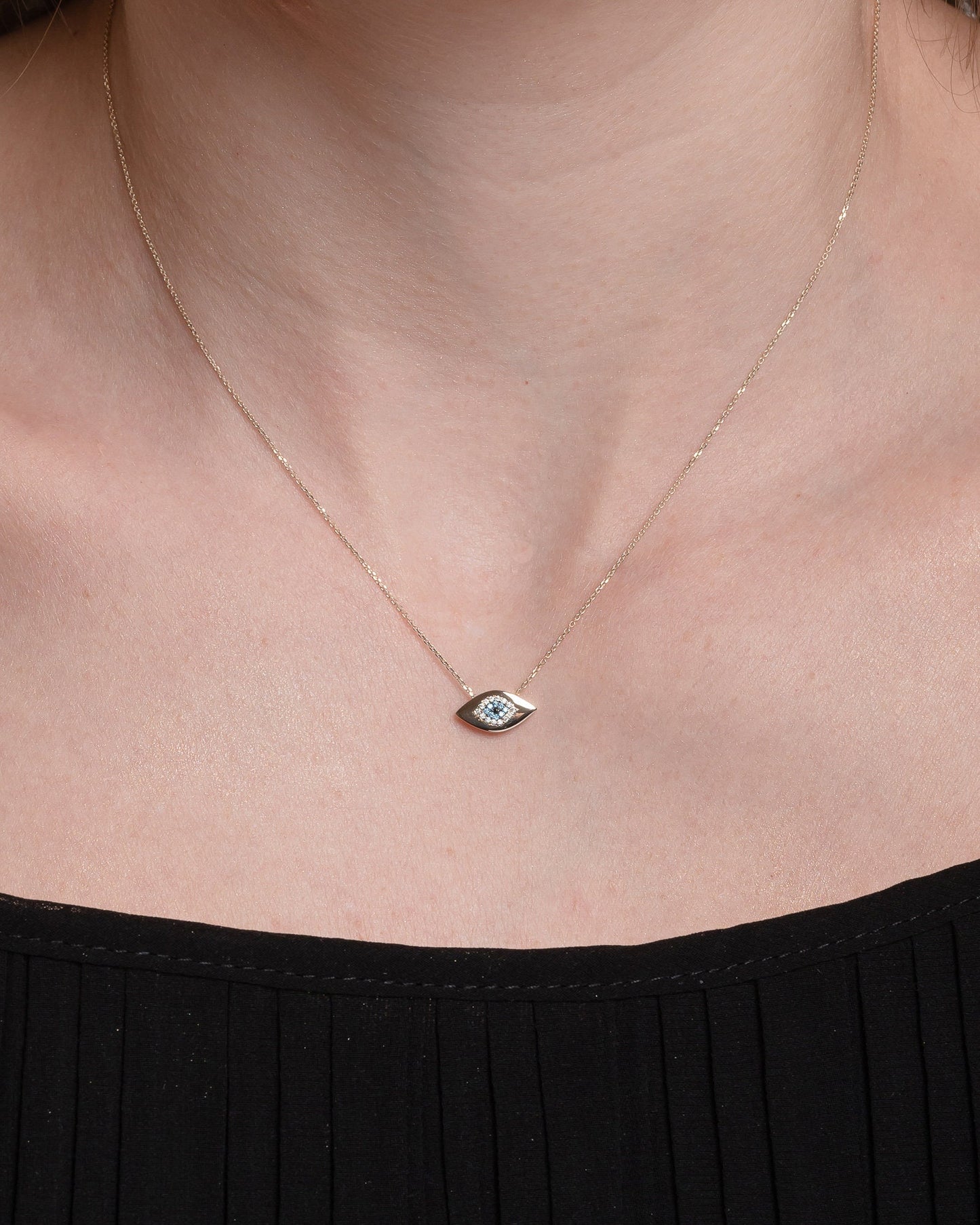 An oval-shaped evil eye necklace crafted in 14k gold and encrusted with cubic zirconia stones worn by a model
