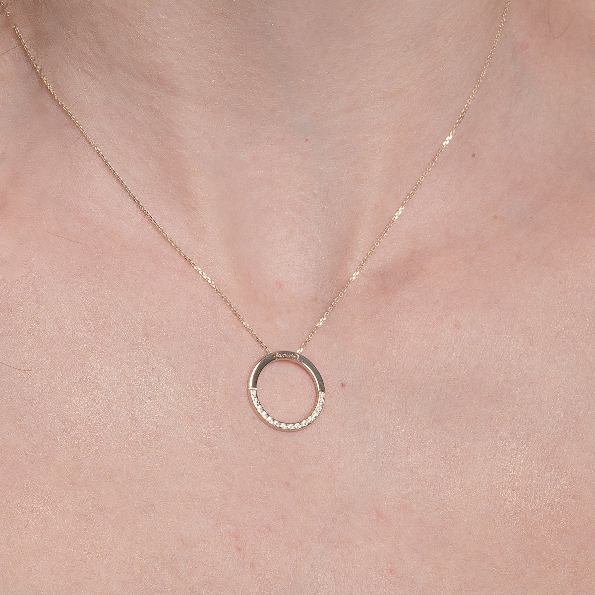 circle karma necklce in 14k gold half of the necklace is paved with cubic zirconia stones worn by a model