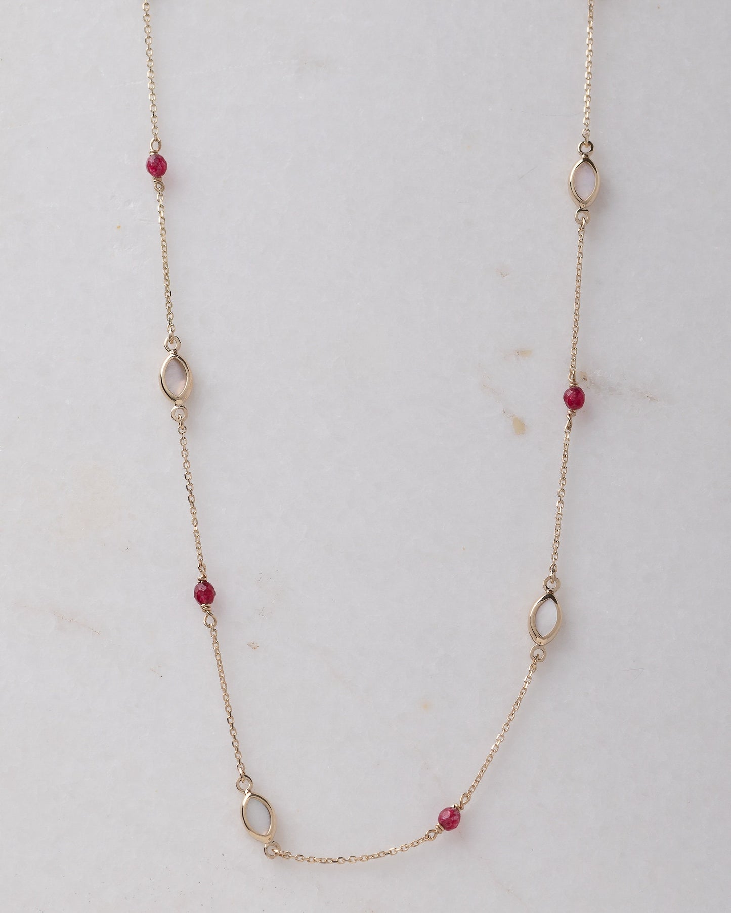 The photo shows a delicate gold necklace featuring small tourmaline gemstones and black marquise-shaped mother of pearl accents, spaced along a fine chain. The contrasting colors create a striking and elegant design