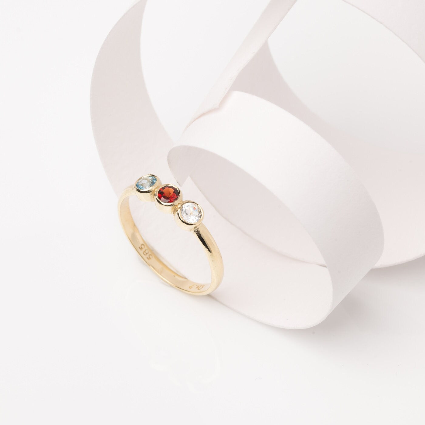 A handmade ring featuring three birthstones set in a bezel, crafted in 14k solid gold.