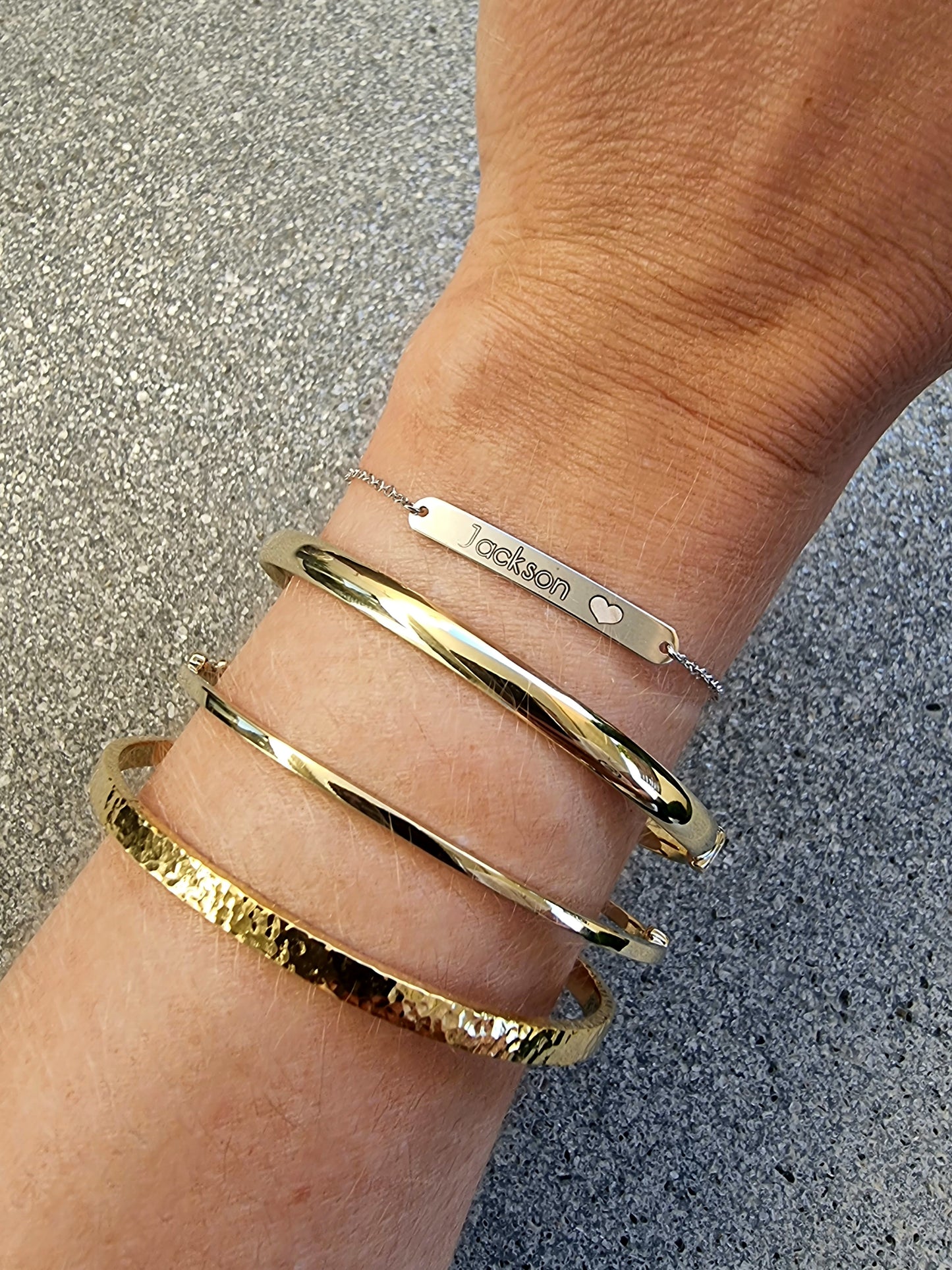 This is an image featuring several gold bracelets on a person's wrist. The bracelets vary in style, a flat bar bracelet, and a couple of bangle designs