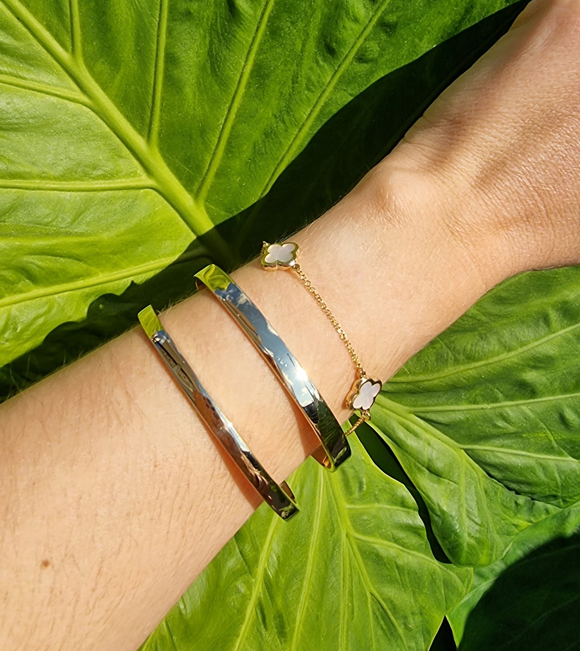 Three bracelets on a wrist: two bangle bracelets and one four-leaf clover bracelet.