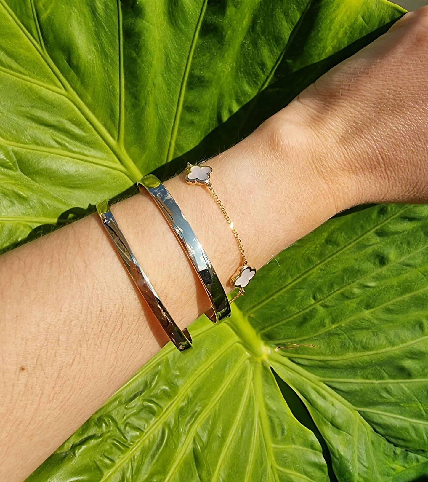 Three bracelets on a wrist: two bangle bracelets and one four-leaf clover bracelet.