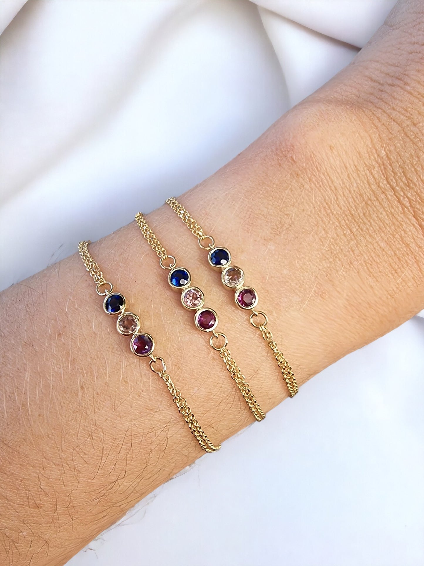 A model wears three 14k gold birthstone bracelets, featuring three stones and a double chain.