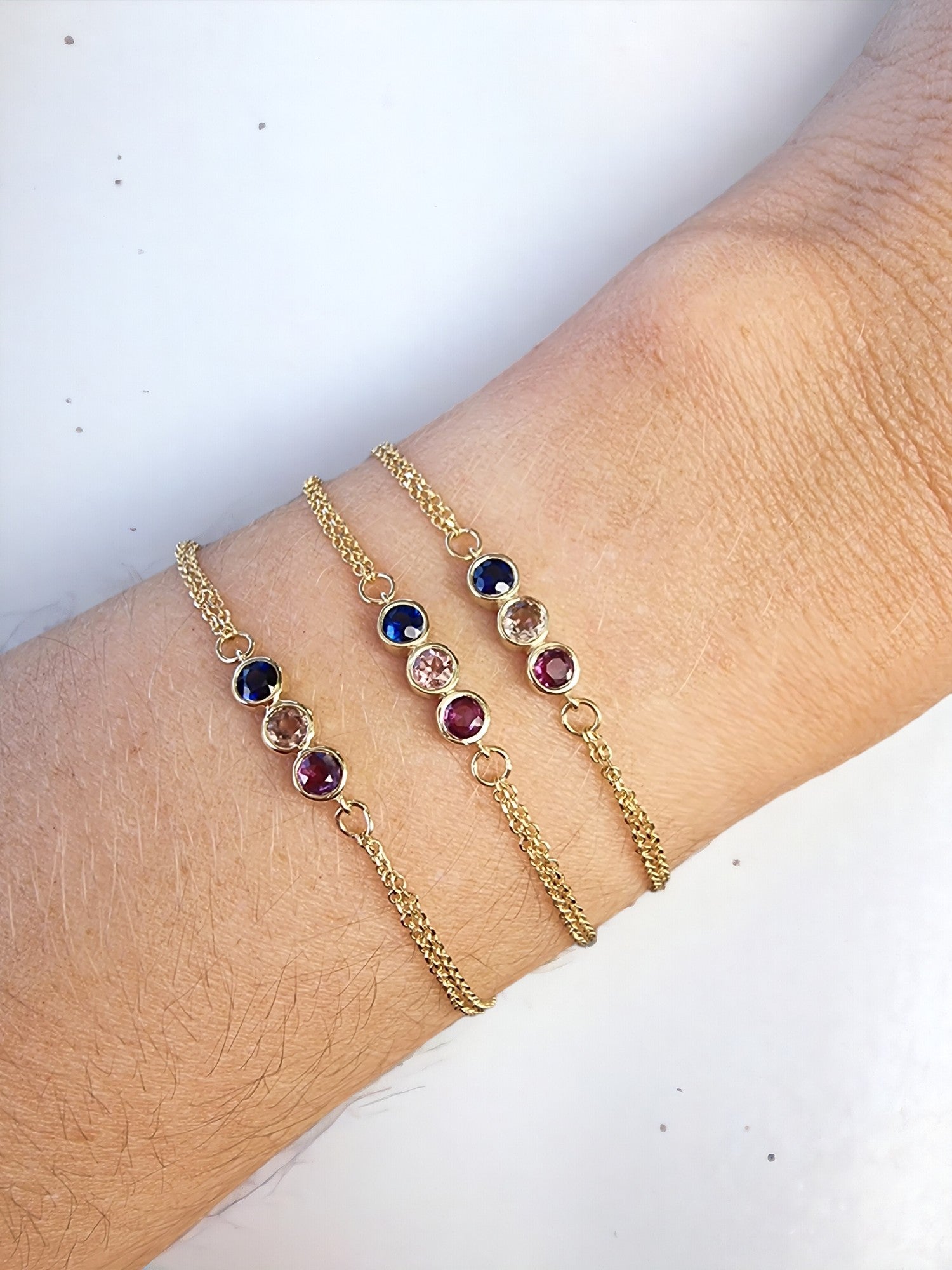 A model wears three 14k gold birthstone bracelets, featuring three stones and a double chain.