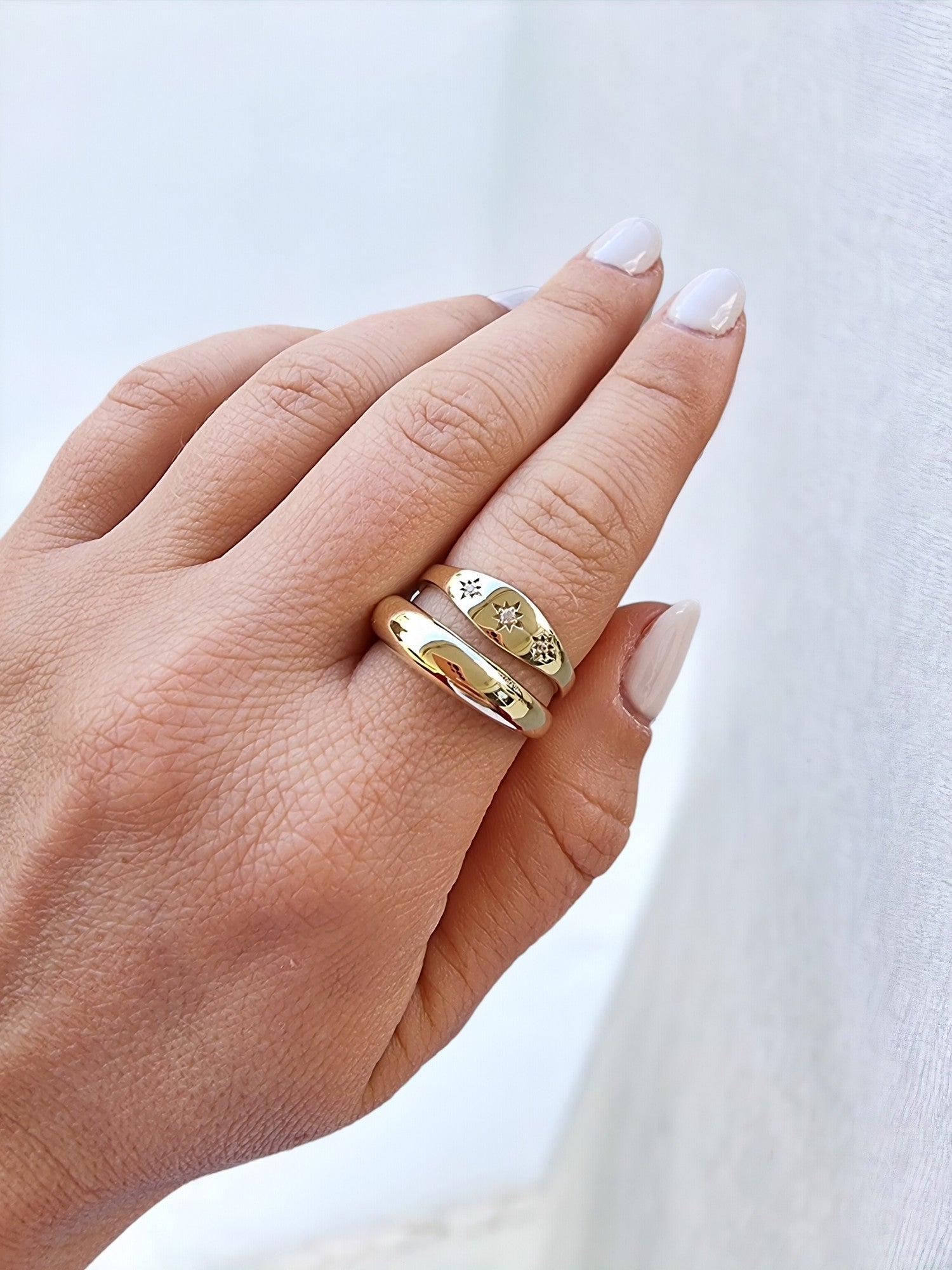 A hand adorned with two rings on the index finger: one, a thick dome ring, and the other, a starburst design.