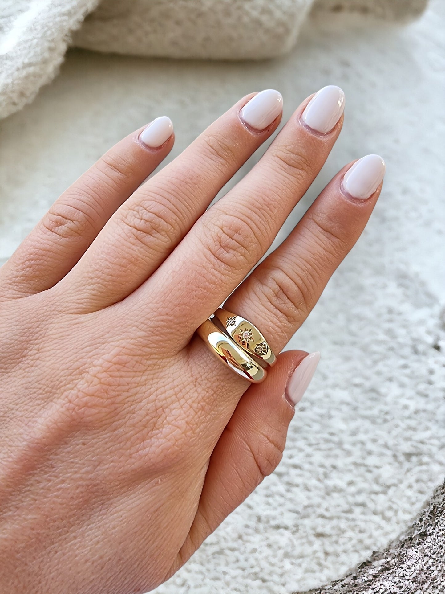 A hand adorned with two rings on the index finger: one, a thick dome ring, and the other, a starburst design.