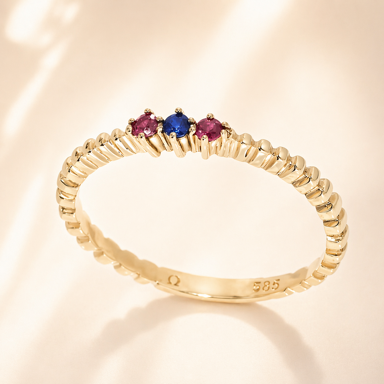 14k Gold ring with three colored gemstones on a beige background