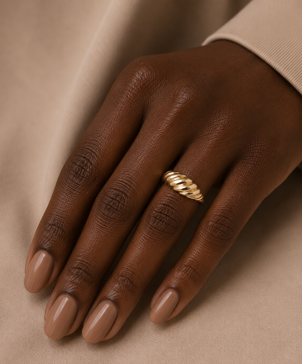 Gold ring on a dark-skinned hand with a neutral background