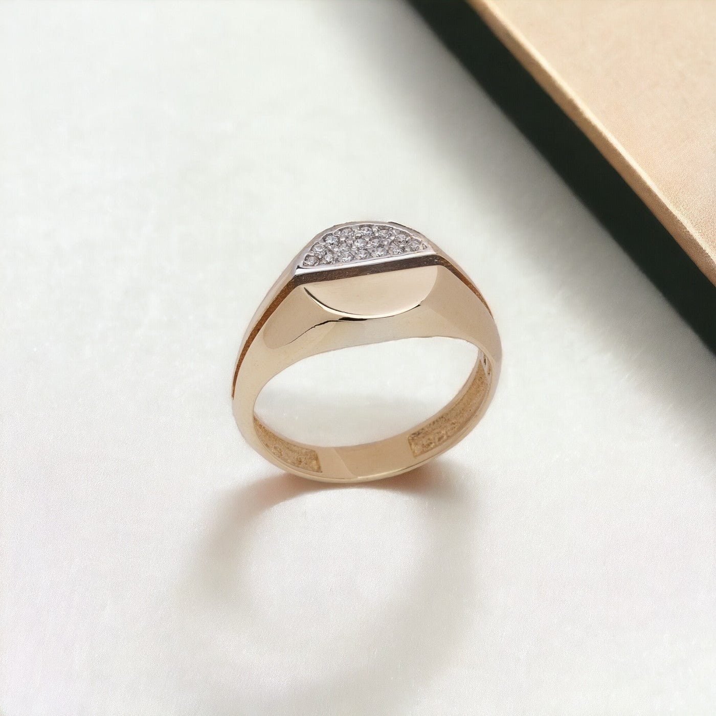 A round signet ring crafted in 14k gold, with half of the top part encrusted with white cubic zirconia stones.