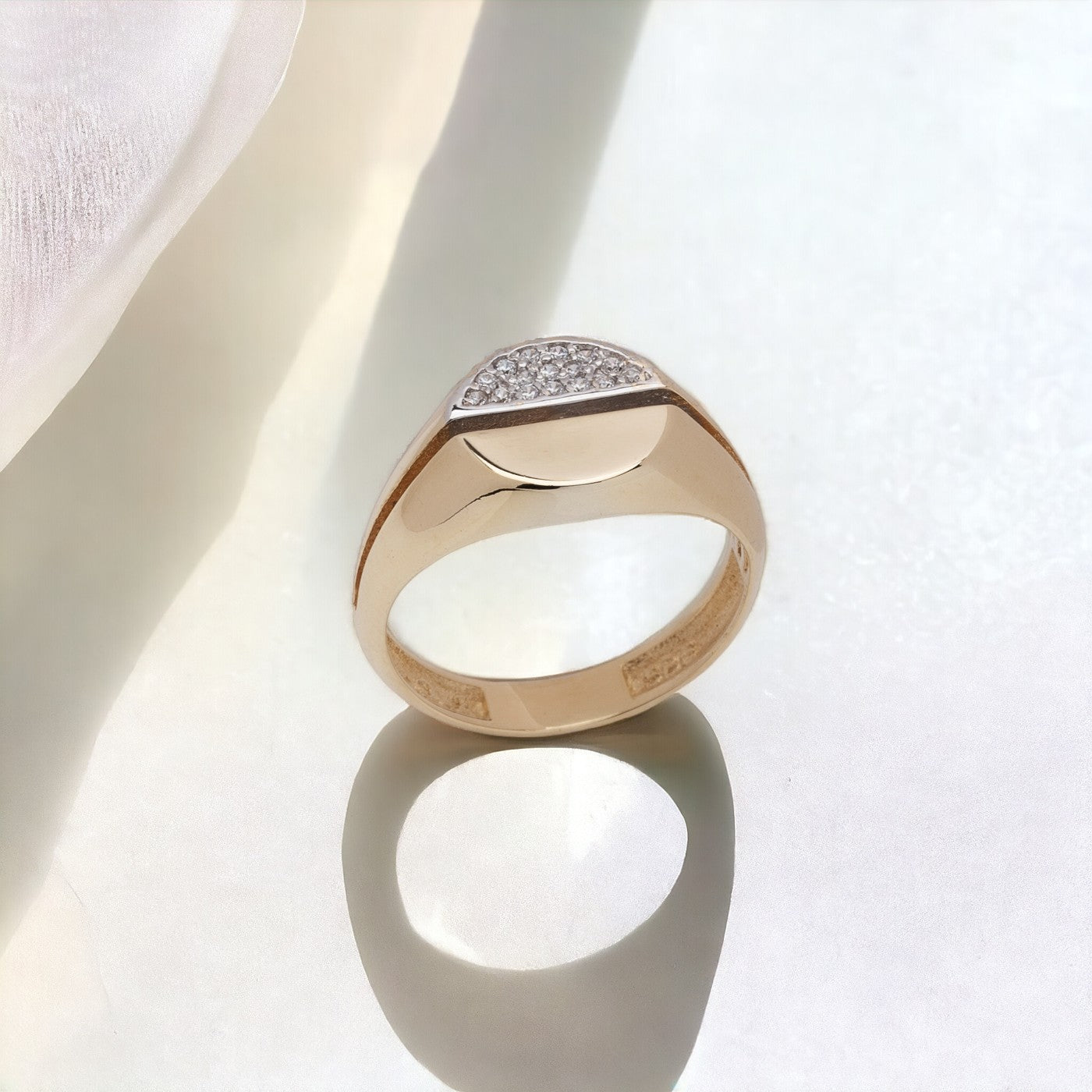 A round signet ring crafted in 14k gold, with half of the top part encrusted with white cubic zirconia stones.