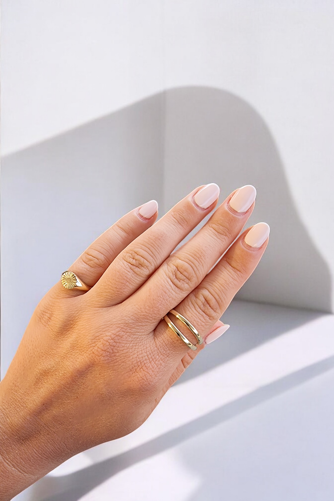 A sun signet ring adorns the pinky finger, while a double row ring is worn on the index finger of a hand.