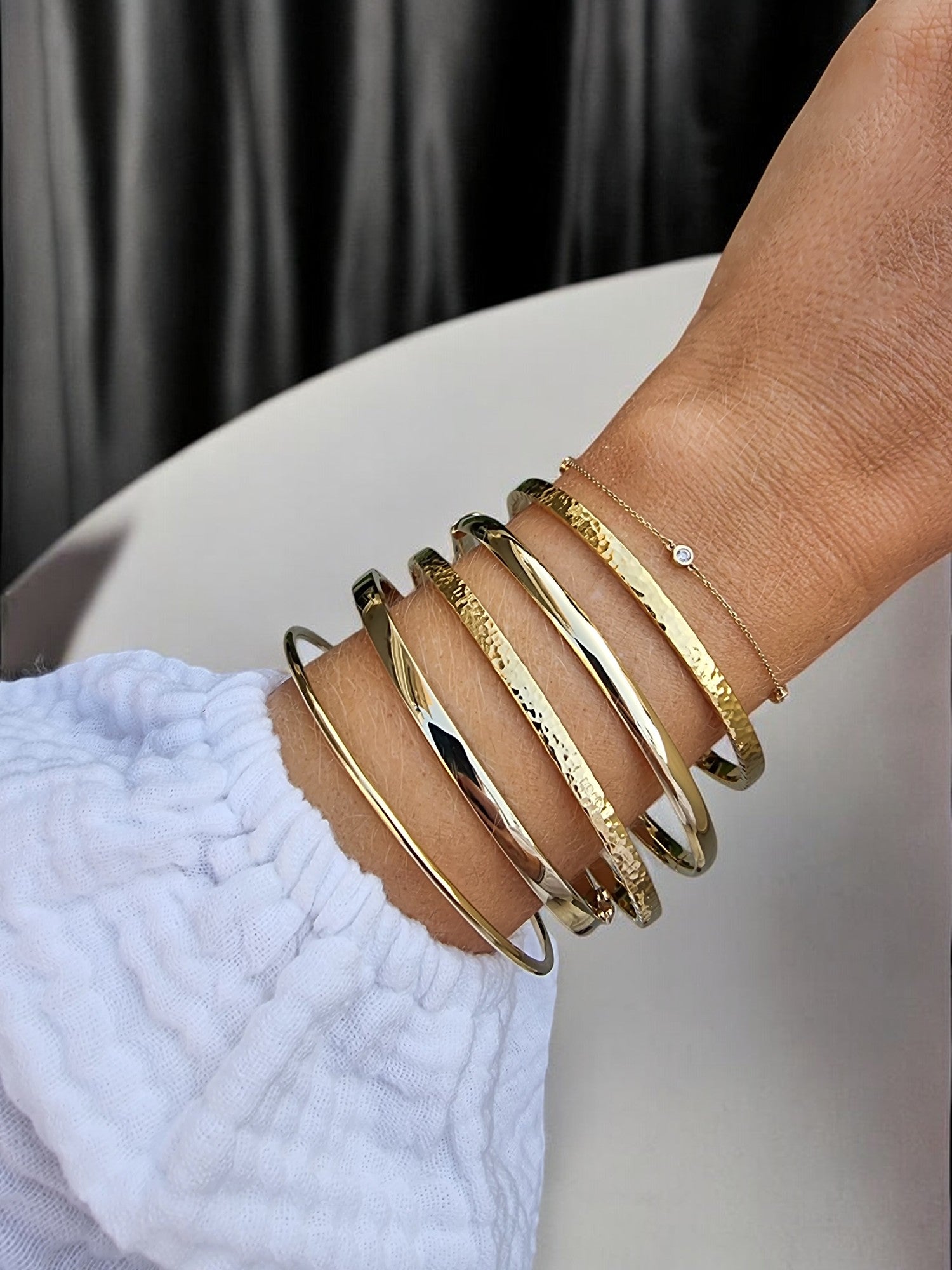 The picture shows a wrist adorned with a variety of gold bracelets.