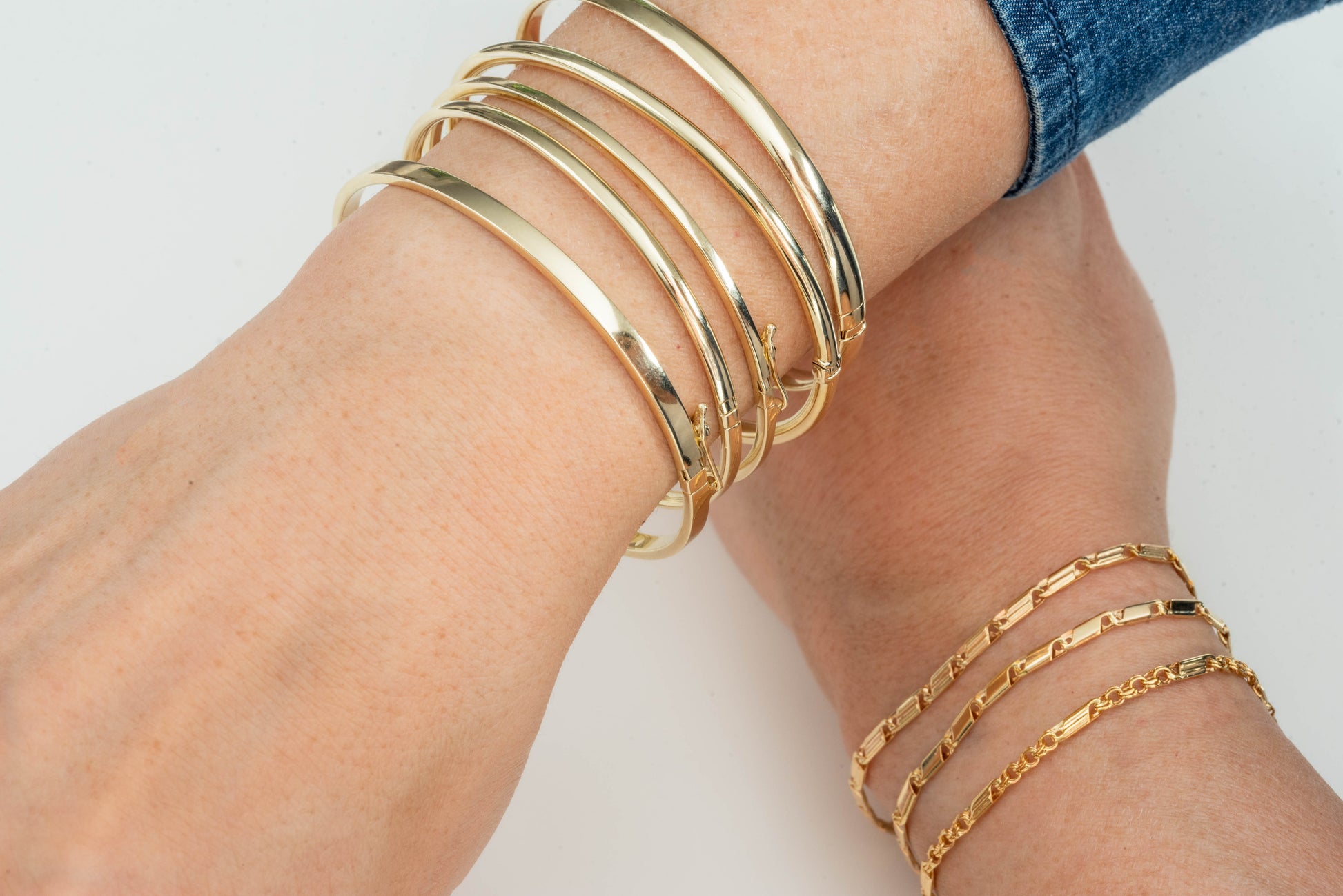 The image shows a close-up of a wrist adorned with several gold bangle bracelets. The person is also wearing a gold ring with small engraved starburst patterns.