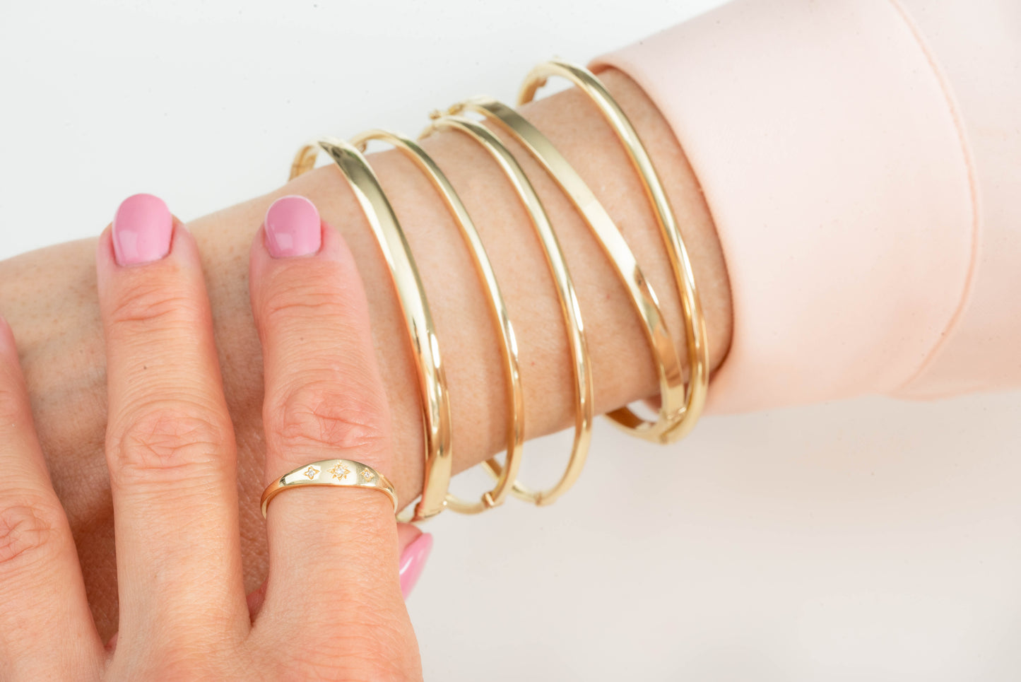 The image shows a close-up of a wrist adorned with several gold bangle bracelets. The person is also wearing a gold ring with small engraved starburst patterns.