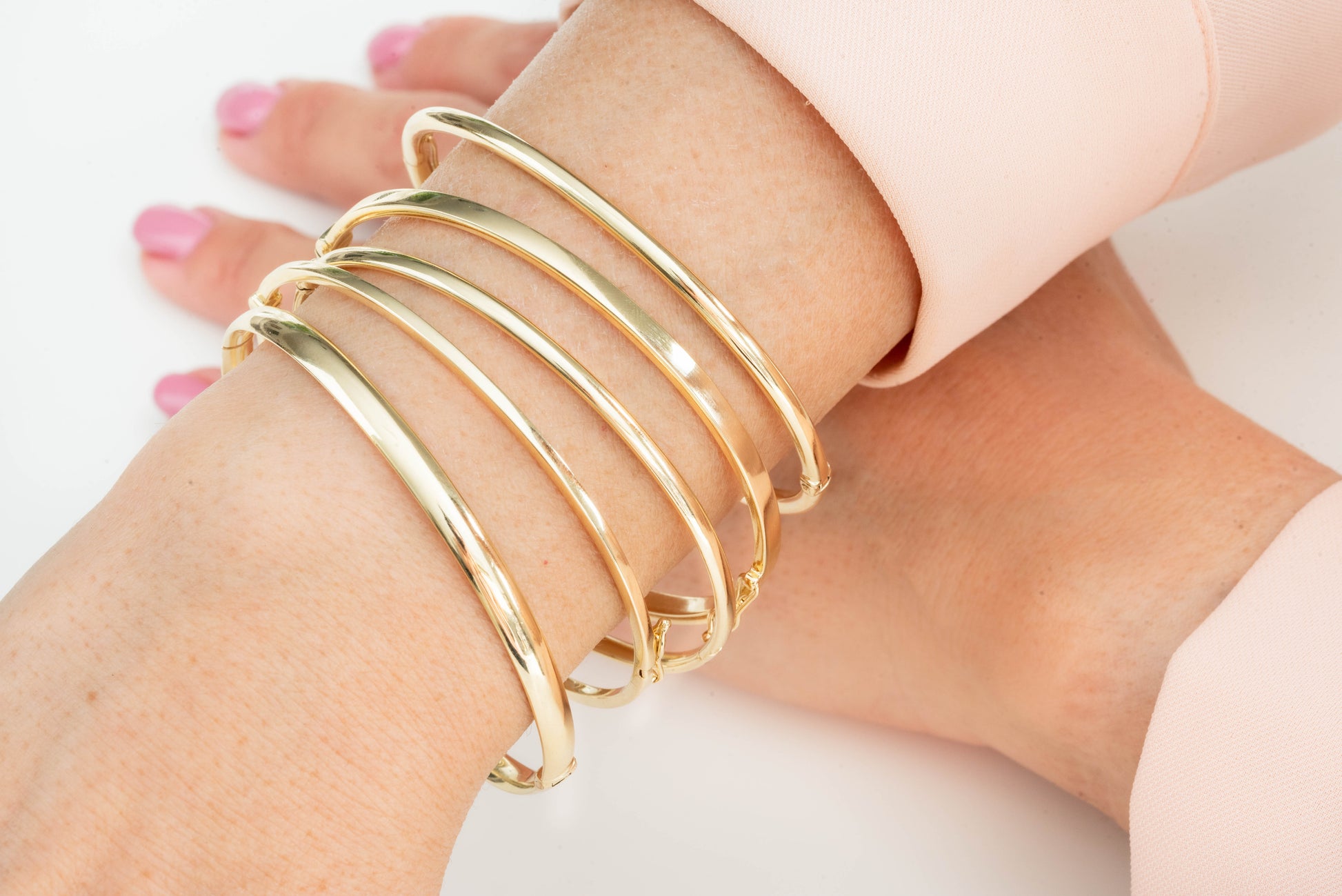 The image shows a close-up of a wrist adorned with several gold bangle bracelets. The person is also wearing a gold ring with small engraved starburst patterns.