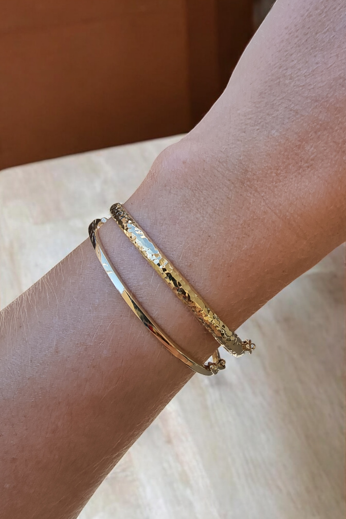 The image shows a wrist adorned with 2 bangle bracelets a hammered texture and one with smooth finish