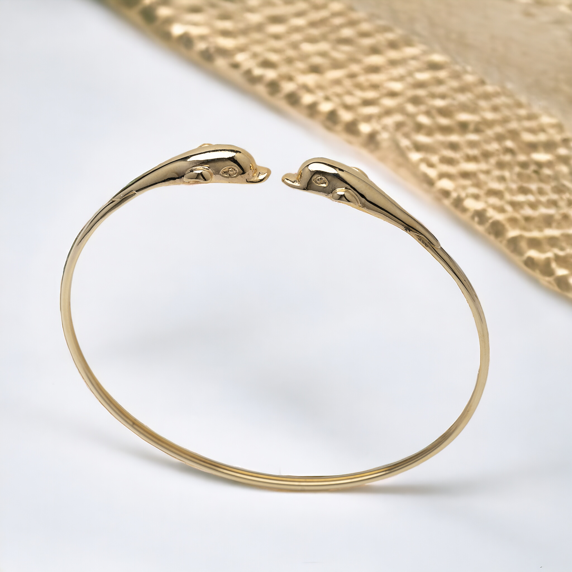 A 14k solid gold bangle bracelet for women, featuring a double dolphin head design.