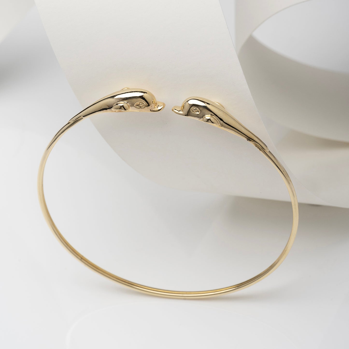 A 14k solid gold bangle bracelet for women, featuring a double dolphin head design.