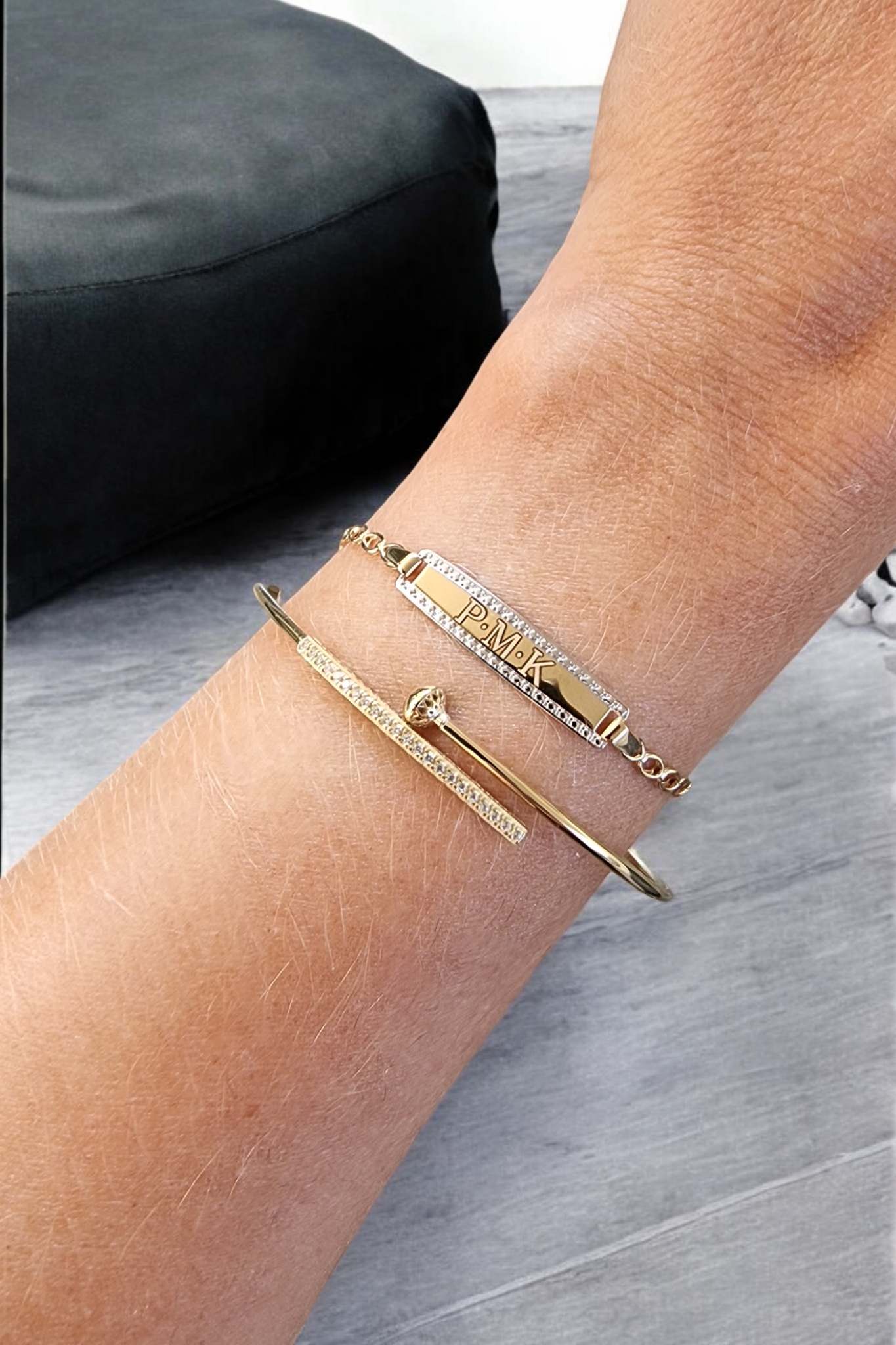 ID bar bracelet in 14k gold that can be engravedalong with a dainty bangle bracelet worn on a wrist