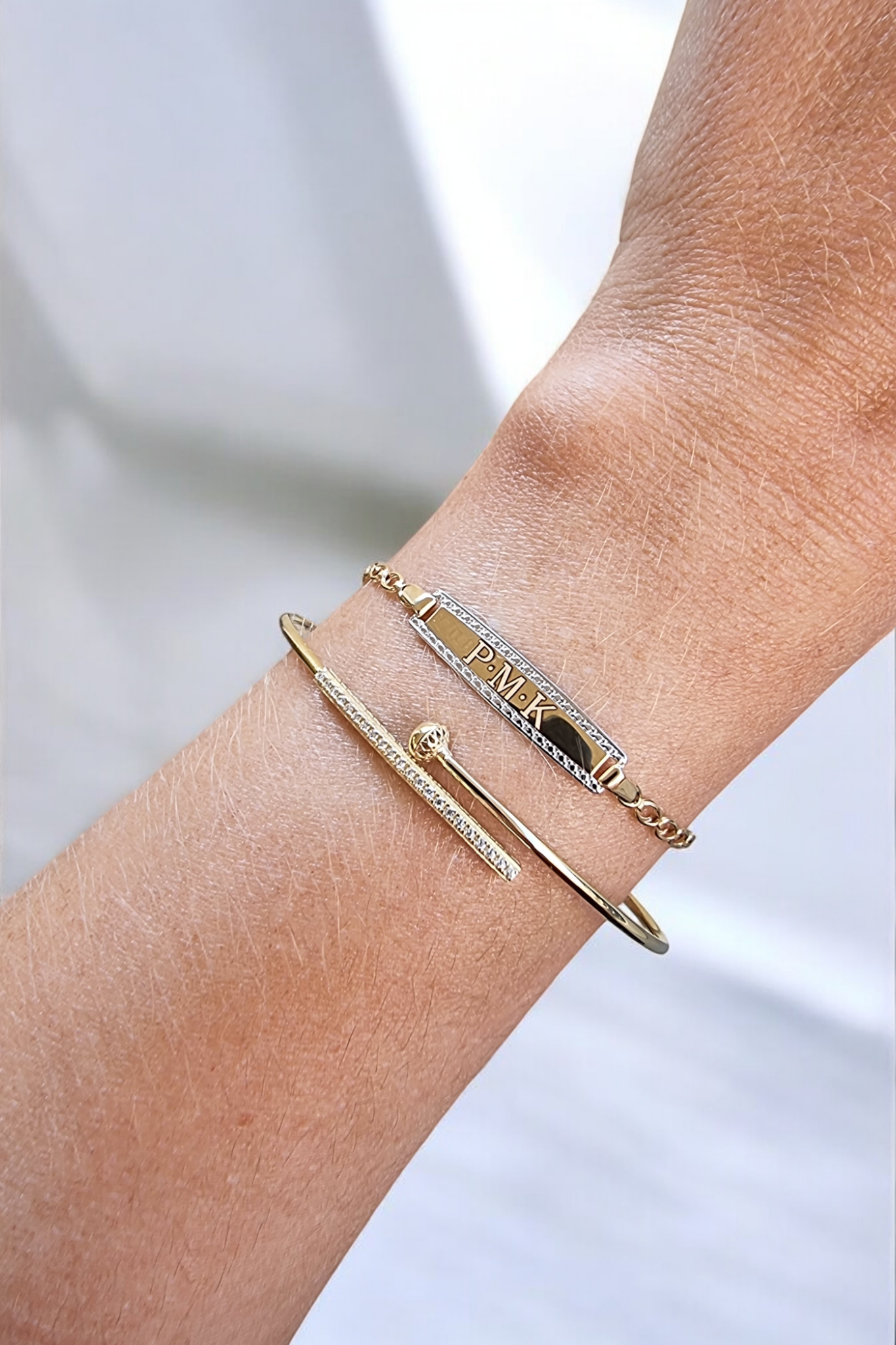 ID bar bracelet in 14k gold that can be engravedalong with a dainty bangle bracelet worn on a wrist