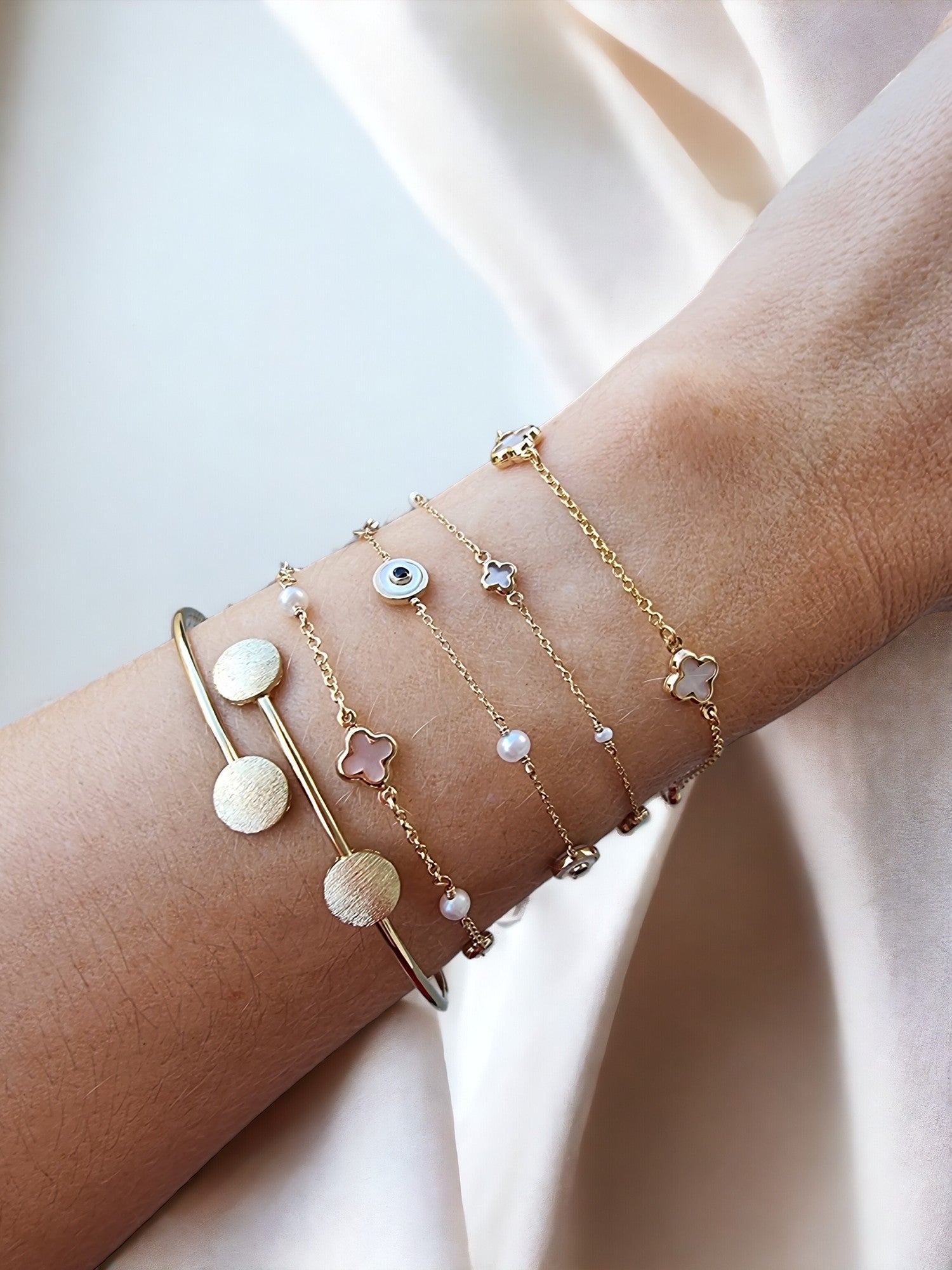 This is an image featuring several gold bracelets on a person's wrist. The bracelets vary in style, including a delicate chain bracelet, and a minimalist bangle design