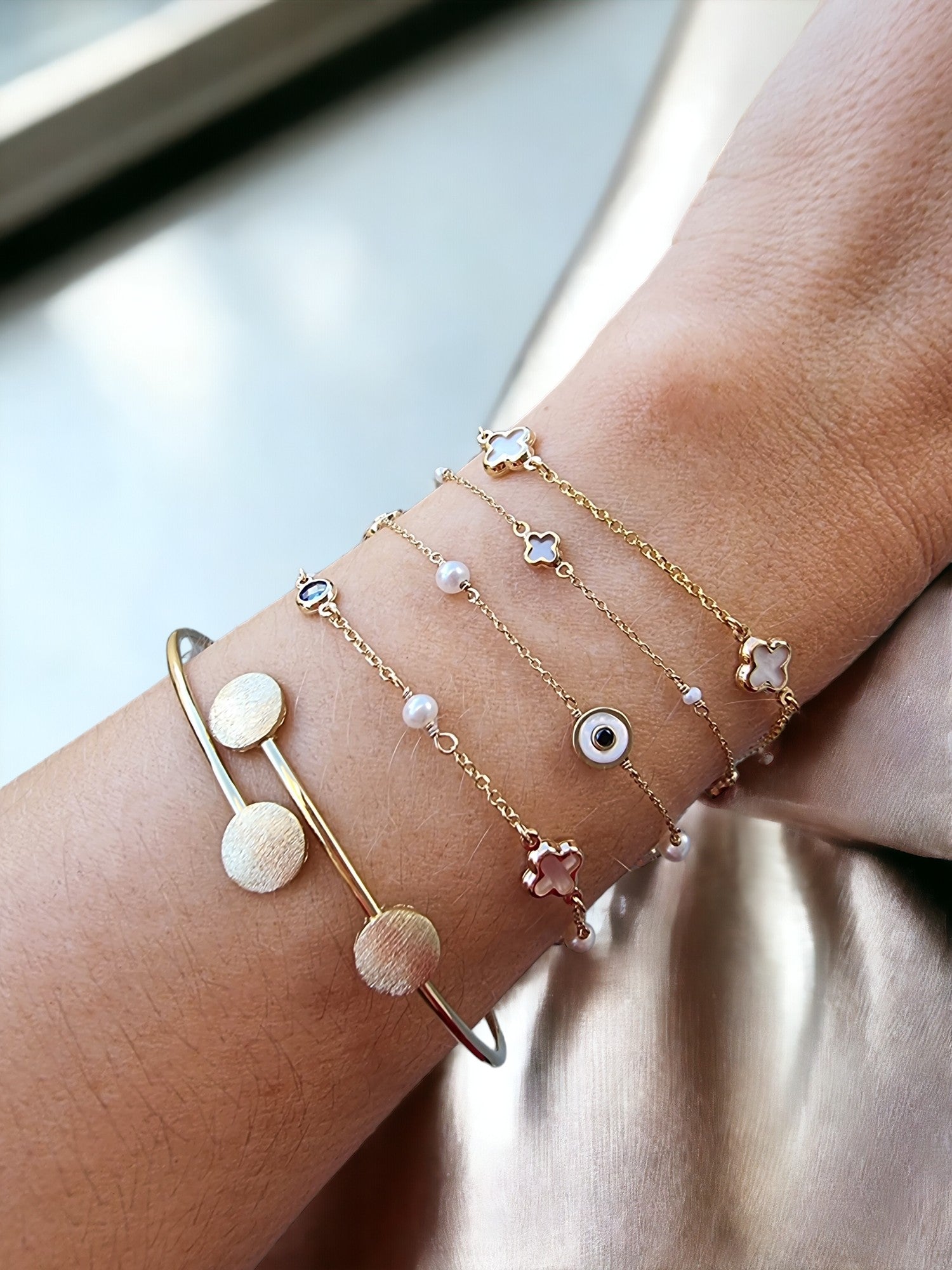 This is an image featuring several gold bracelets on a person's wrist. The bracelets vary in style, including a delicate chain bracelet, and a minimalist bangle design