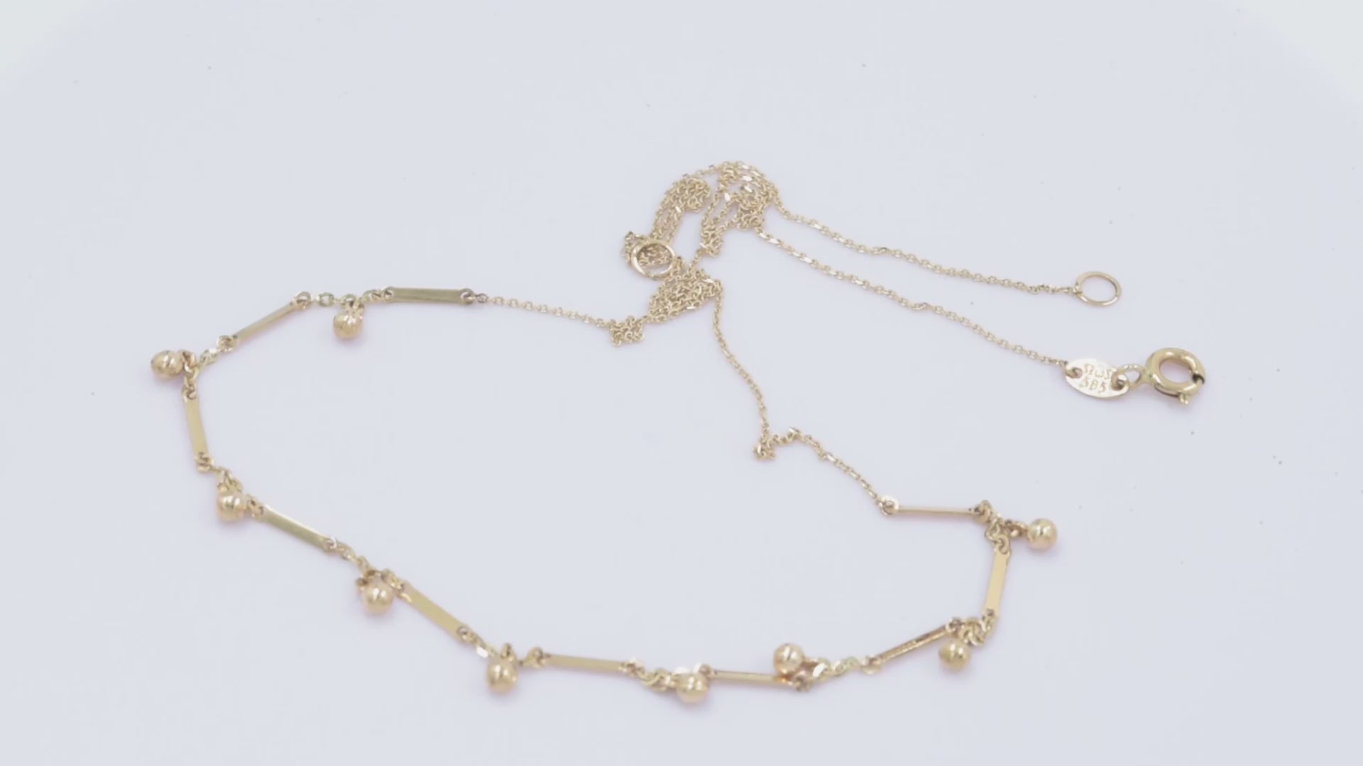  a gold necklace featuring small, shiny, spherical bead-like pendants spaced along a fine chain. Between the beads, there are slim, rectangular bar accents.