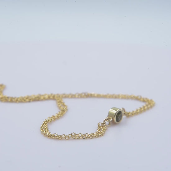 A handmade bracelet featuring a single birthstone in a bezel setting, crafted in 14k gold with a double chain design.