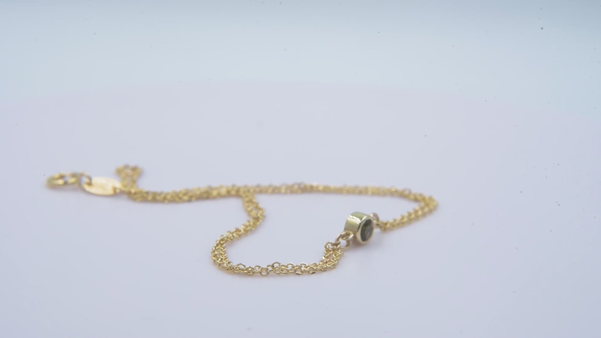 A handmade bracelet featuring a single birthstone in a bezel setting, crafted in 14k gold with a double chain design.