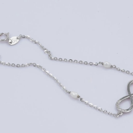 A women's bracelet featuring the infinity symbol in 14k white gold, adorned with cubic zirconia stones and pearls.