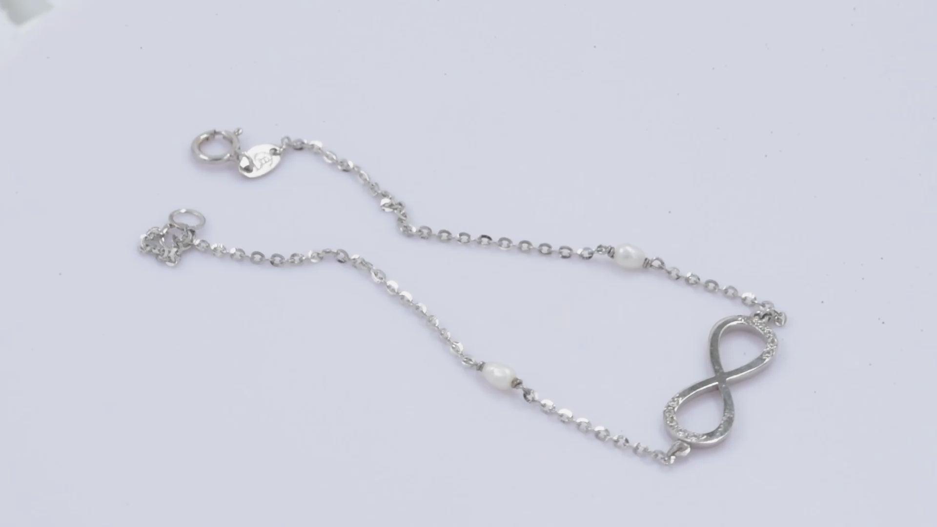 A women's bracelet featuring the infinity symbol in 14k white gold, adorned with cubic zirconia stones and pearls.