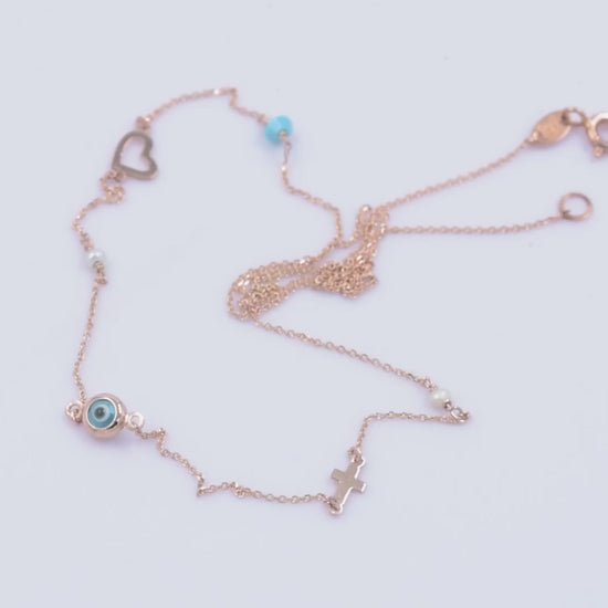 A station necklace featuring an evil eye, heart, cross, pearls, and a turquoise stone, all crafted in 14k gold.