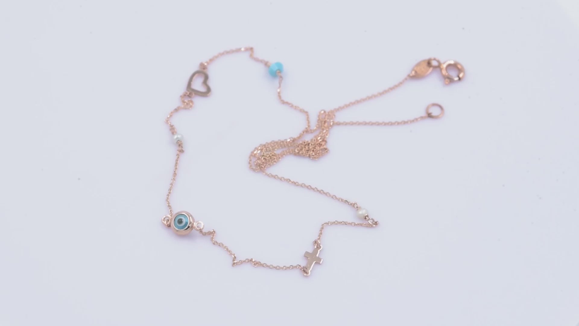 A station necklace featuring an evil eye, heart, cross, pearls, and a turquoise stone, all crafted in 14k gold.