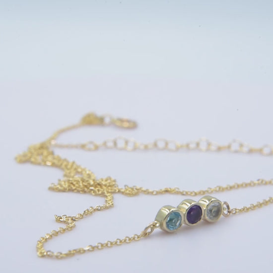 A 14k gold birthstone necklace for women, featuring three stones in a bezel setting.