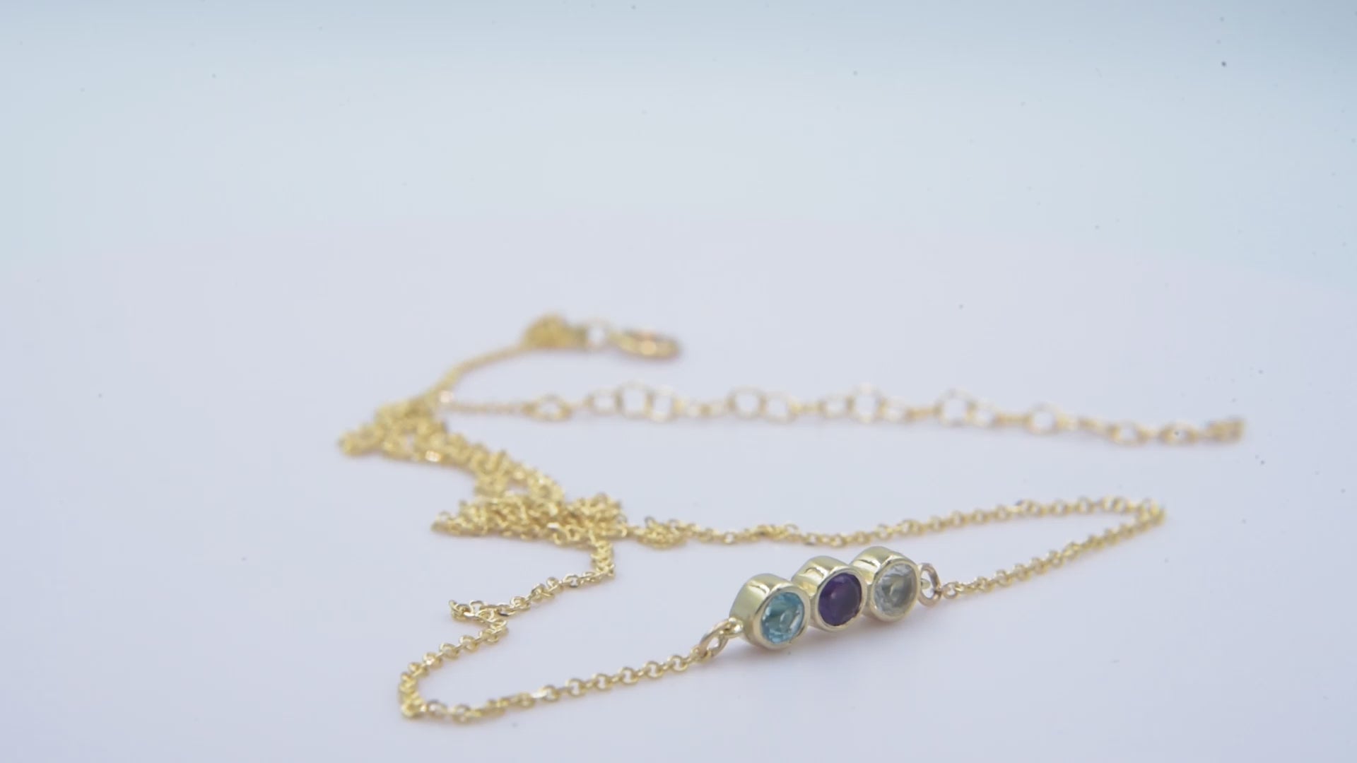 A 14k gold birthstone necklace for women, featuring three stones in a bezel setting.