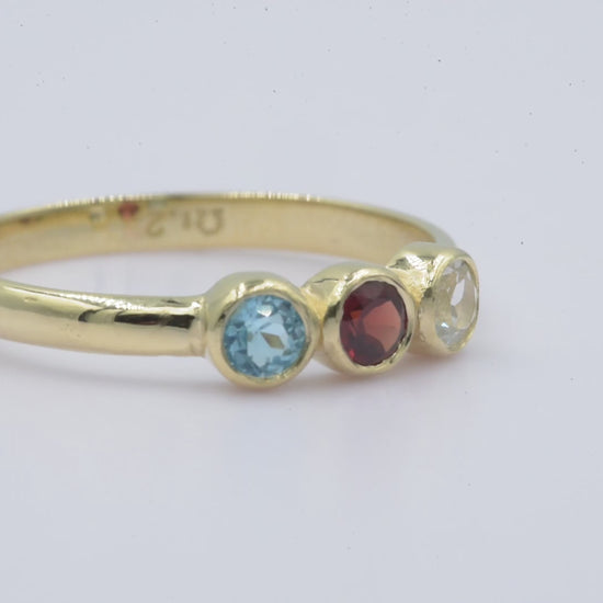 A handmade ring featuring three birthstones set in a bezel, crafted in 14k solid gold.