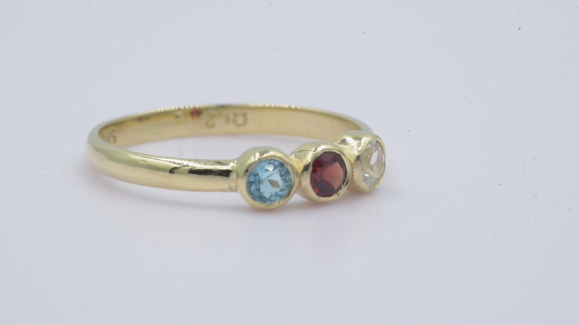 A handmade ring featuring three birthstones set in a bezel, crafted in 14k solid gold.