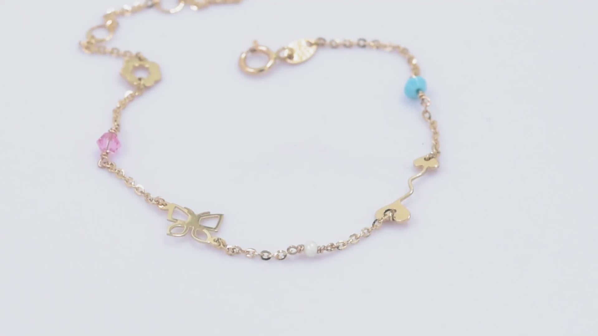 A 14k gold charm bracelet featuring an arrow, a flower, a butterfly, and three colorful gemstones.