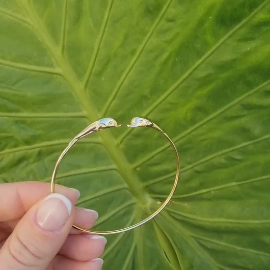 A 14k solid gold bangle bracelet for women, featuring a double dolphin head design.